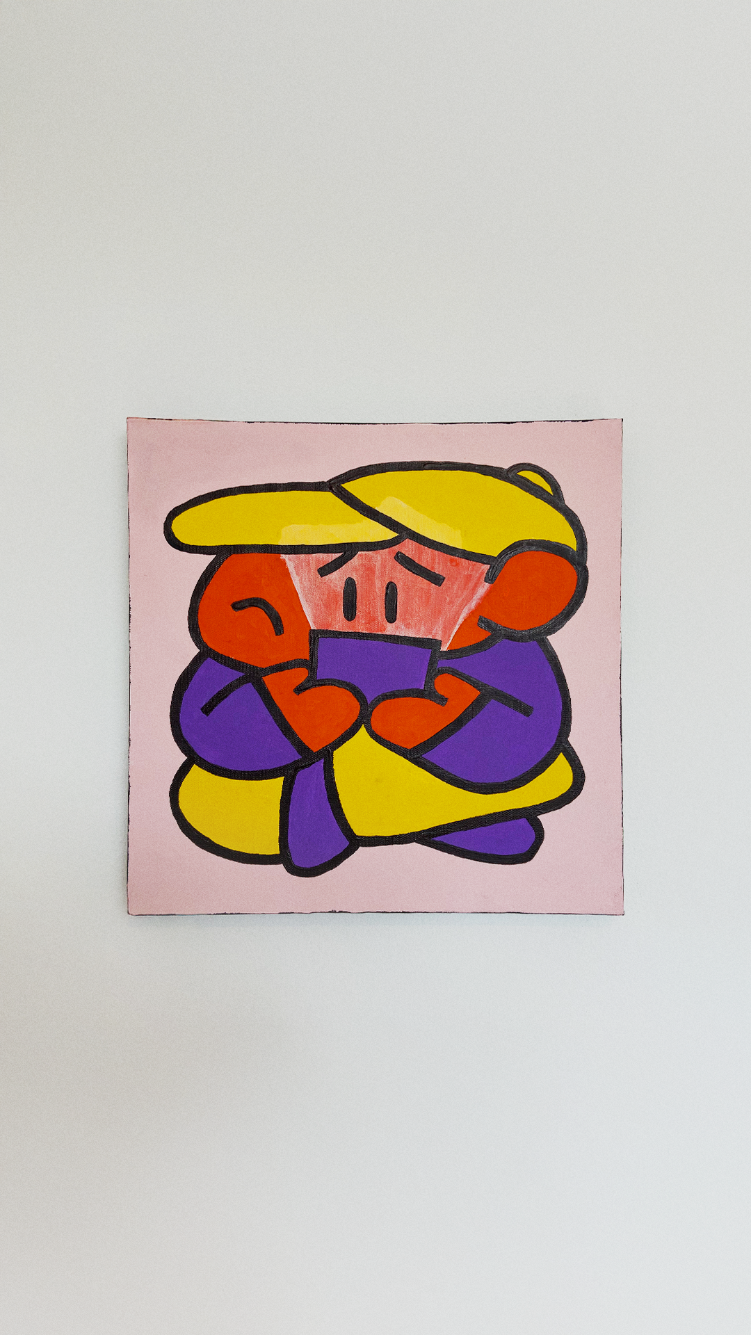 A small orange character wearing a yellow cap and purple clothing and holding a purple book on a pink canvas.