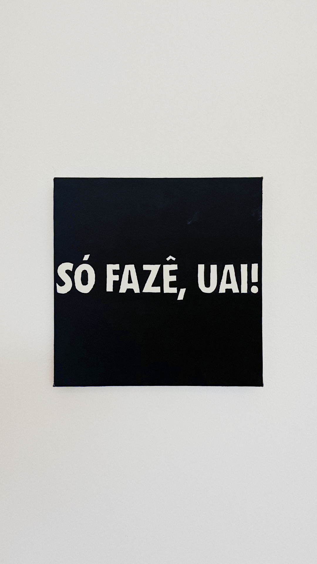White Portuguese lettering reading 'Só fazê, uai!' on a black acrylic-painted canvas.