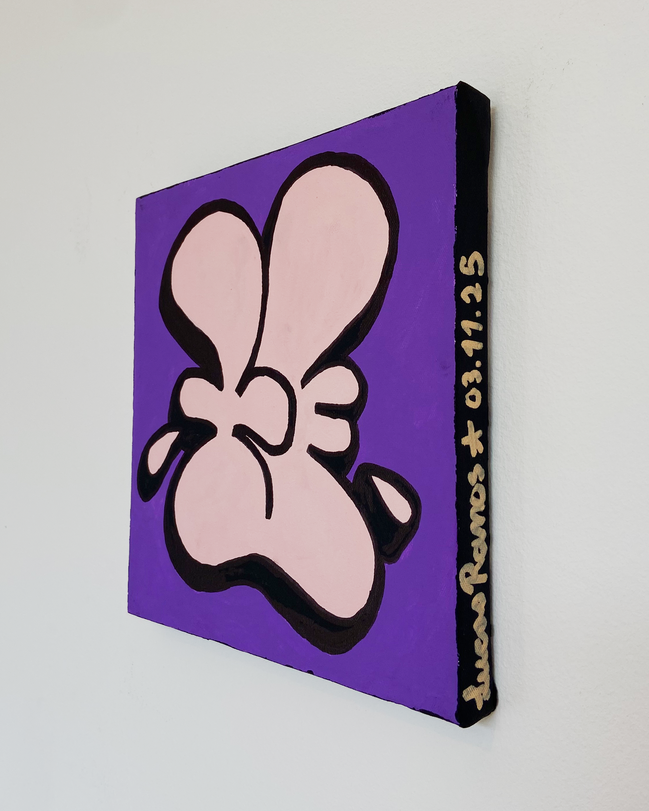 Angled view of the Nice Studio acrylic painting showing the pink and black symbol on purple canvas and Lucas Ramos' signature and completion date on the black right edge.