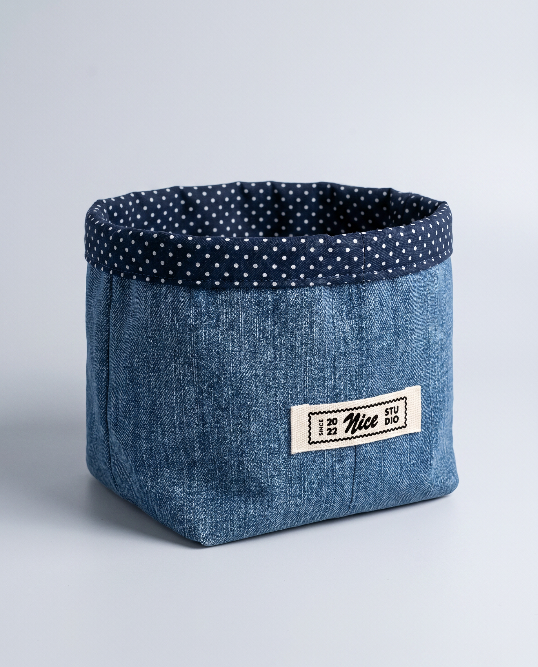 Three-quarter view of the denim cachepot, showing its soft-sided form, folded rim, and Nice Studio label.